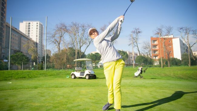 Woman in bright attire swinging a golf club on a sunny day in Portugal.