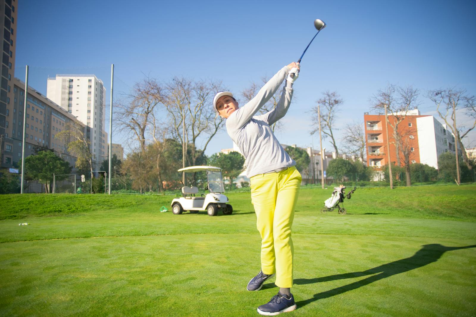 Woman in bright attire swinging a golf club on a sunny day in Portugal.